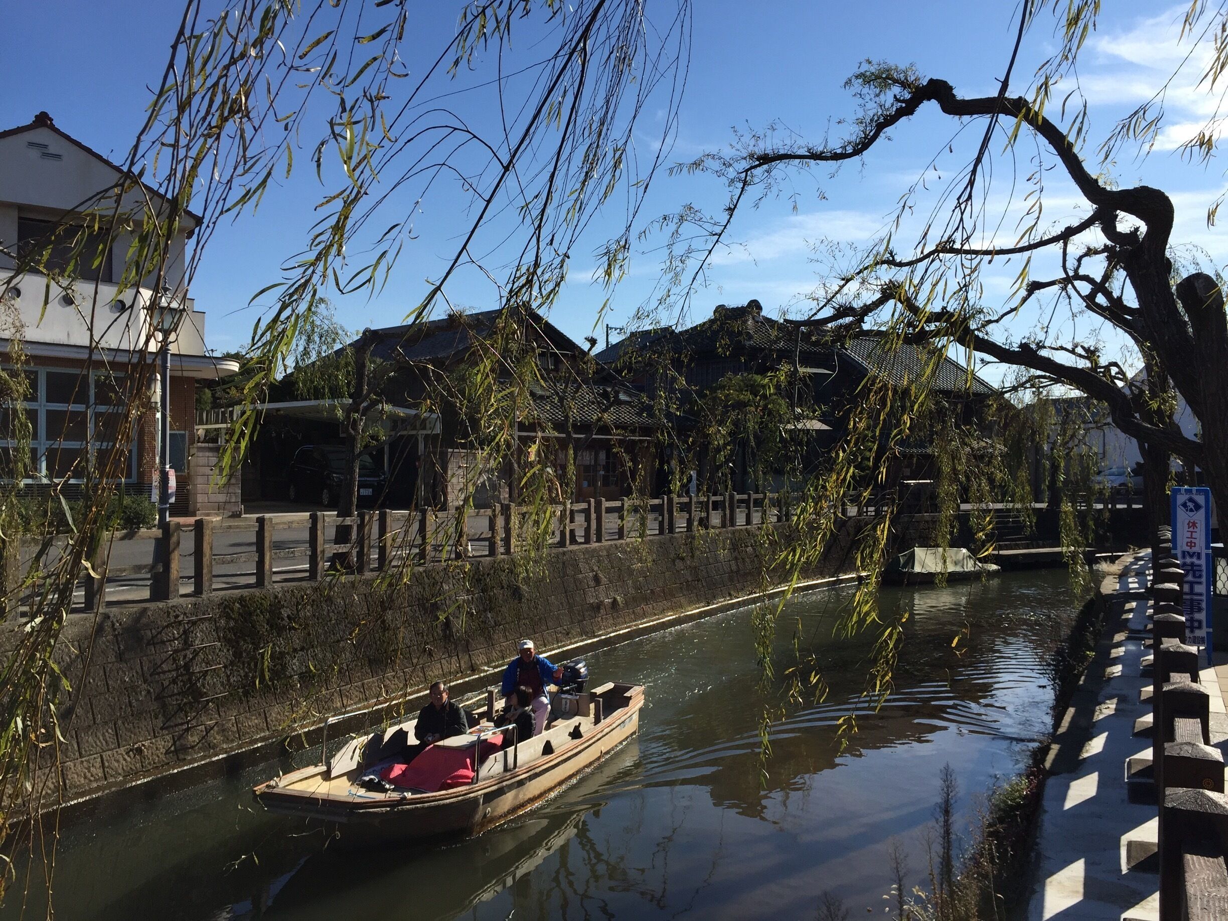 A traditional wooden boat on a canal with buildings and trees in the background.