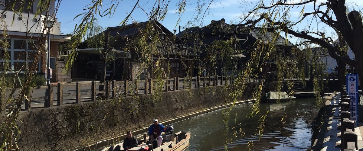 A traditional wooden boat on a canal with buildings and trees in the background.