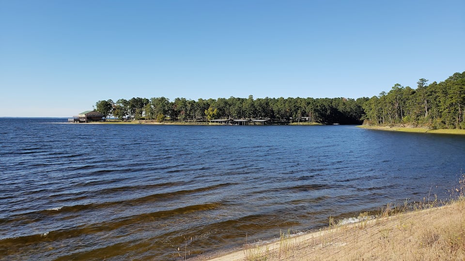 A lake with a sandy shore, a forested island, and a small building.