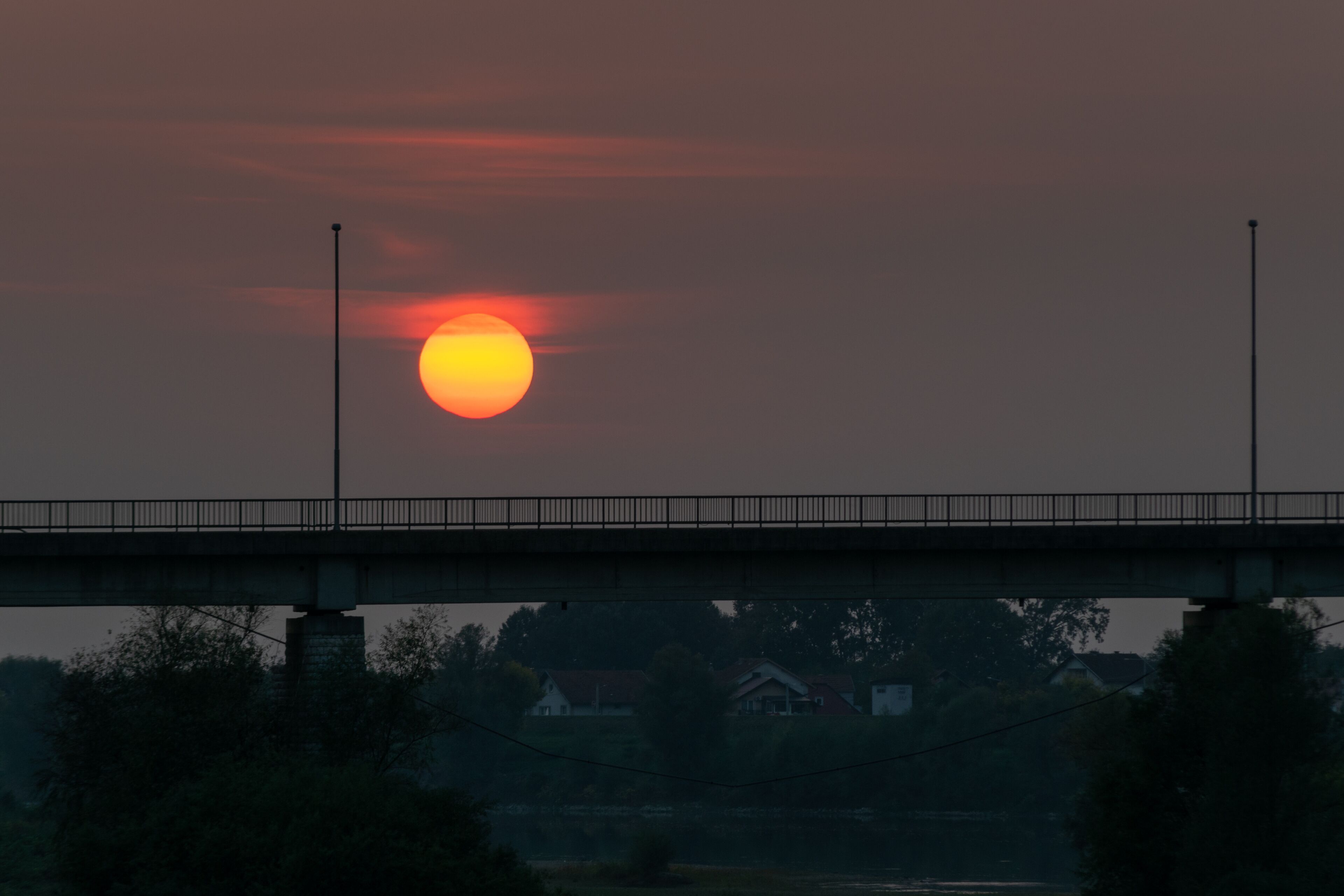 Silhouette of the bridge on the river Sava between Bosnia and Herzegovina and Croatia against a cloudy sky with a big orange sun