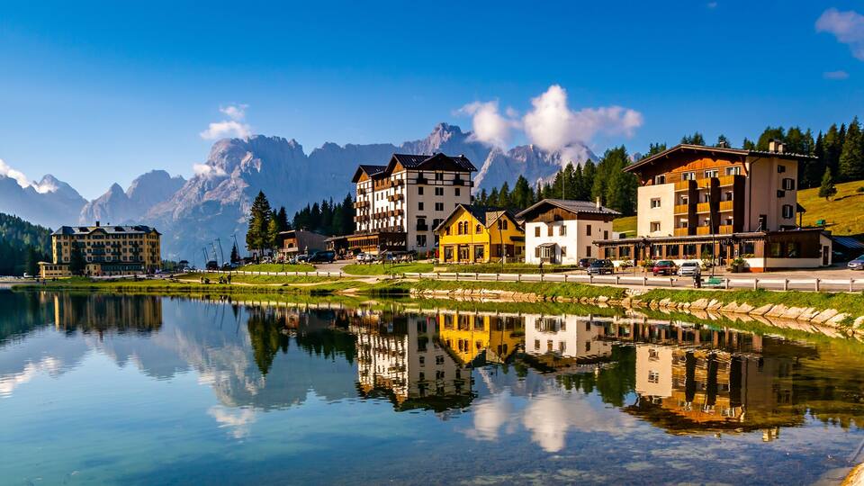 A lakeside town with buildings reflecting in the water, surrounded by mountains.