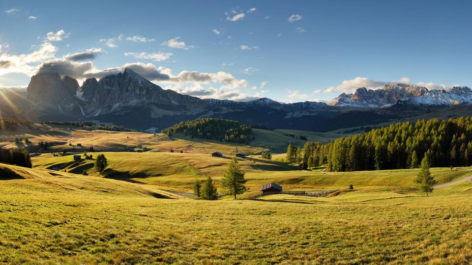 A mountainous landscape with a small cabin, rolling hills, and a clear sky.