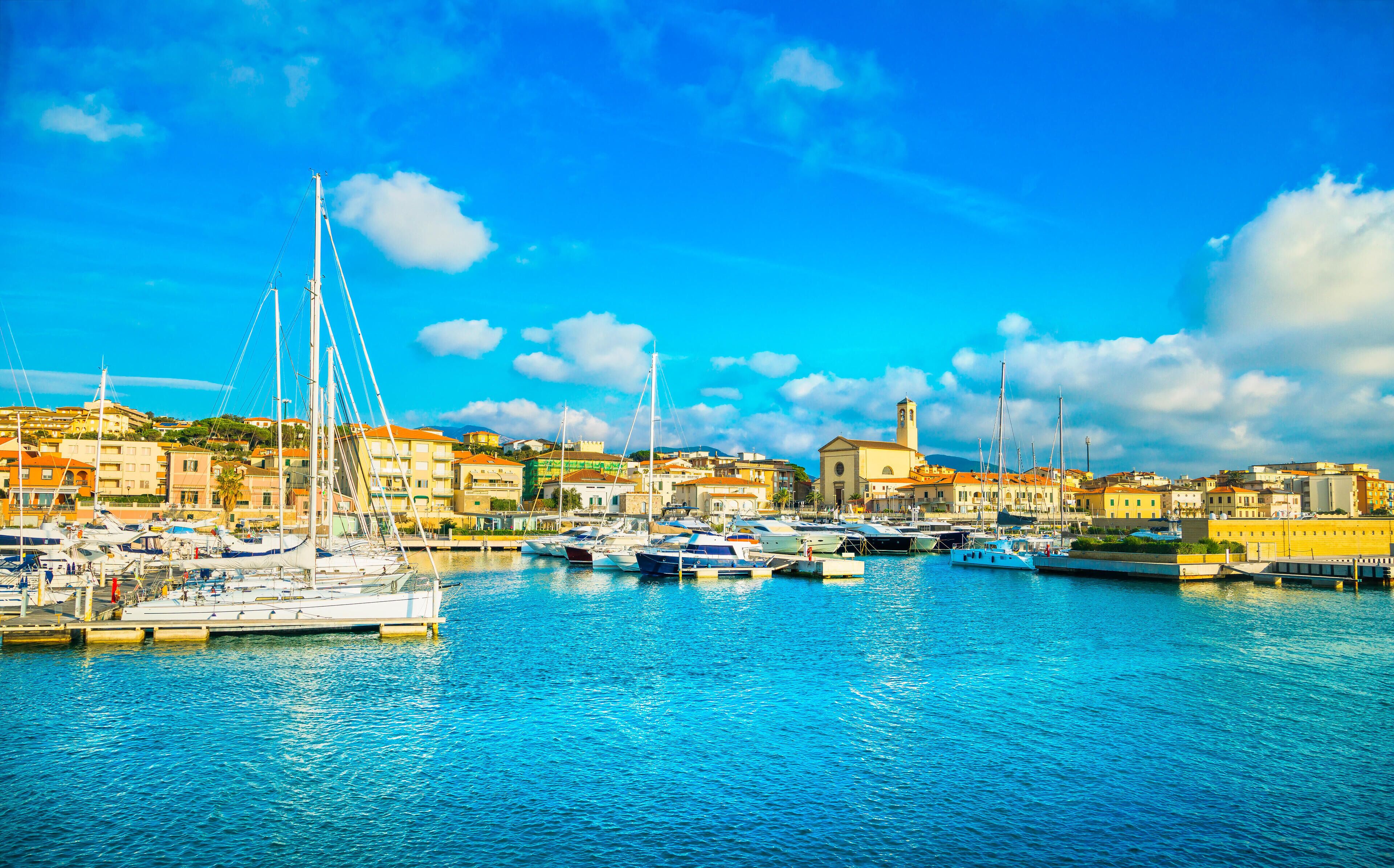 A marina with boats docked, a clear blue sky, and buildings in the background.