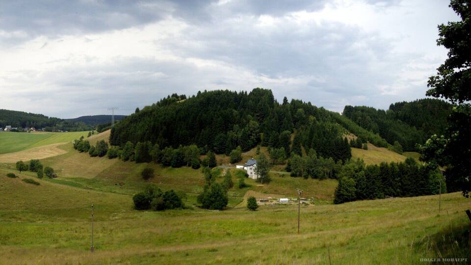A rural landscape with rolling hills, scattered houses, and dense forests.