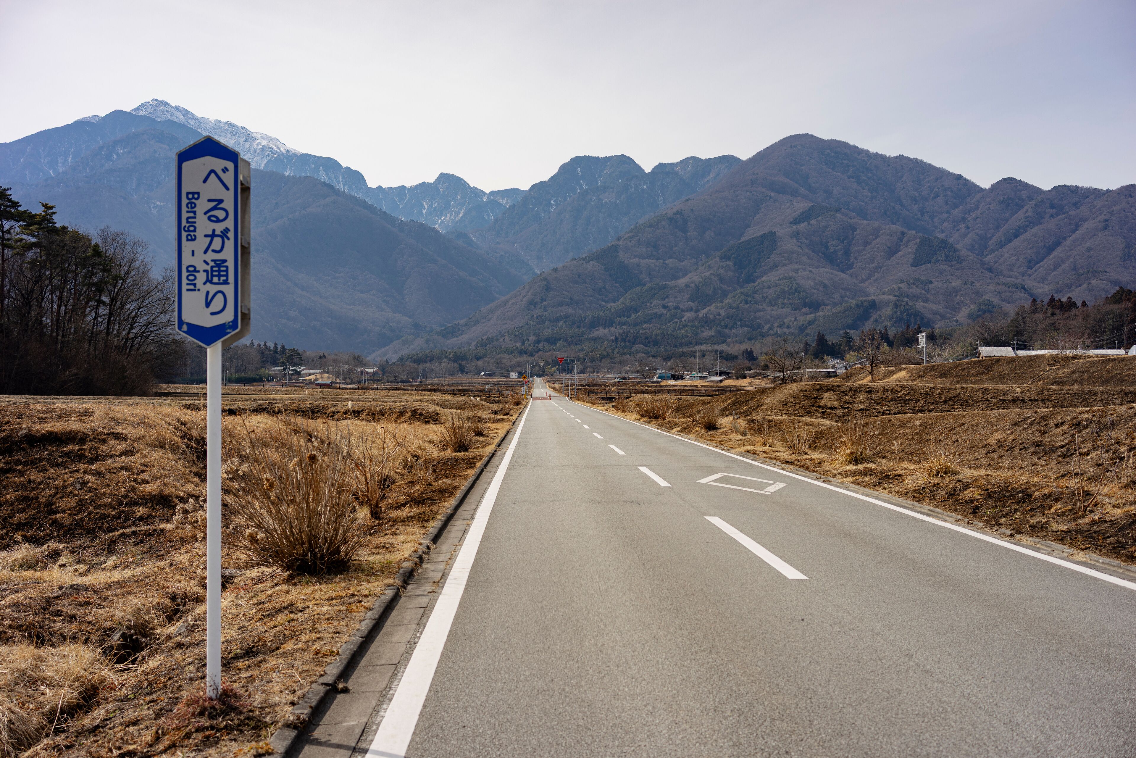 A road with a sign in Japanese, surrounded by mountains and dry grass.