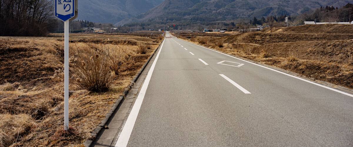 A road with a sign in Japanese, surrounded by mountains and dry grass.