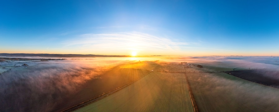 A sunrise over a vast landscape with fields and a road.