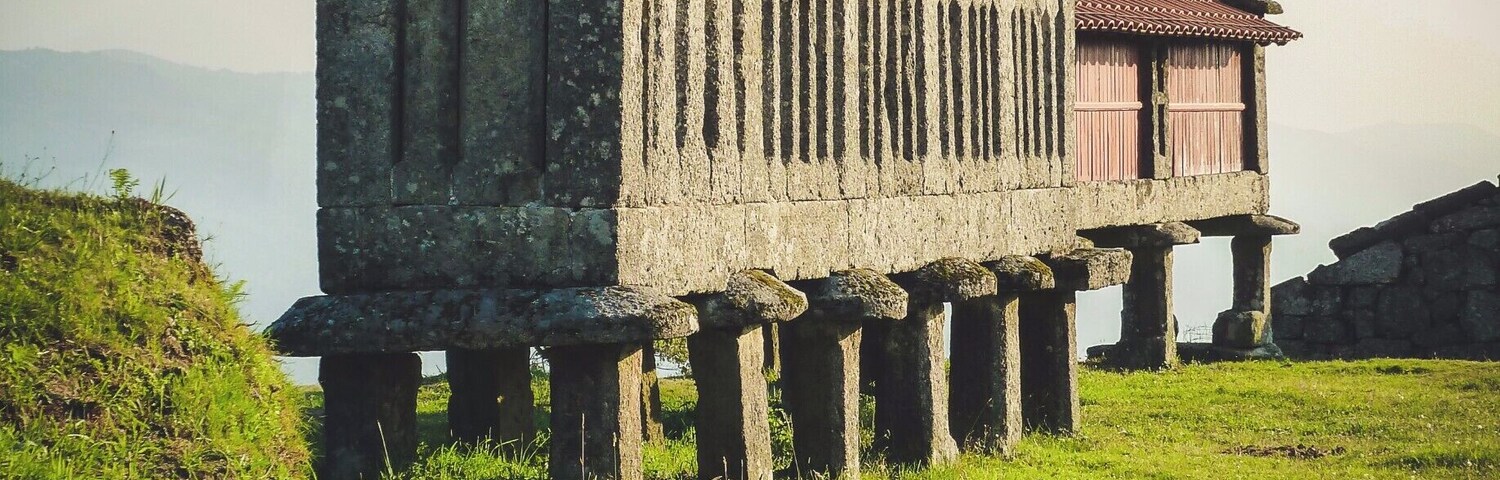 Una capilla de piedra con cruces en la parte superior, rodeada de césped y colinas.