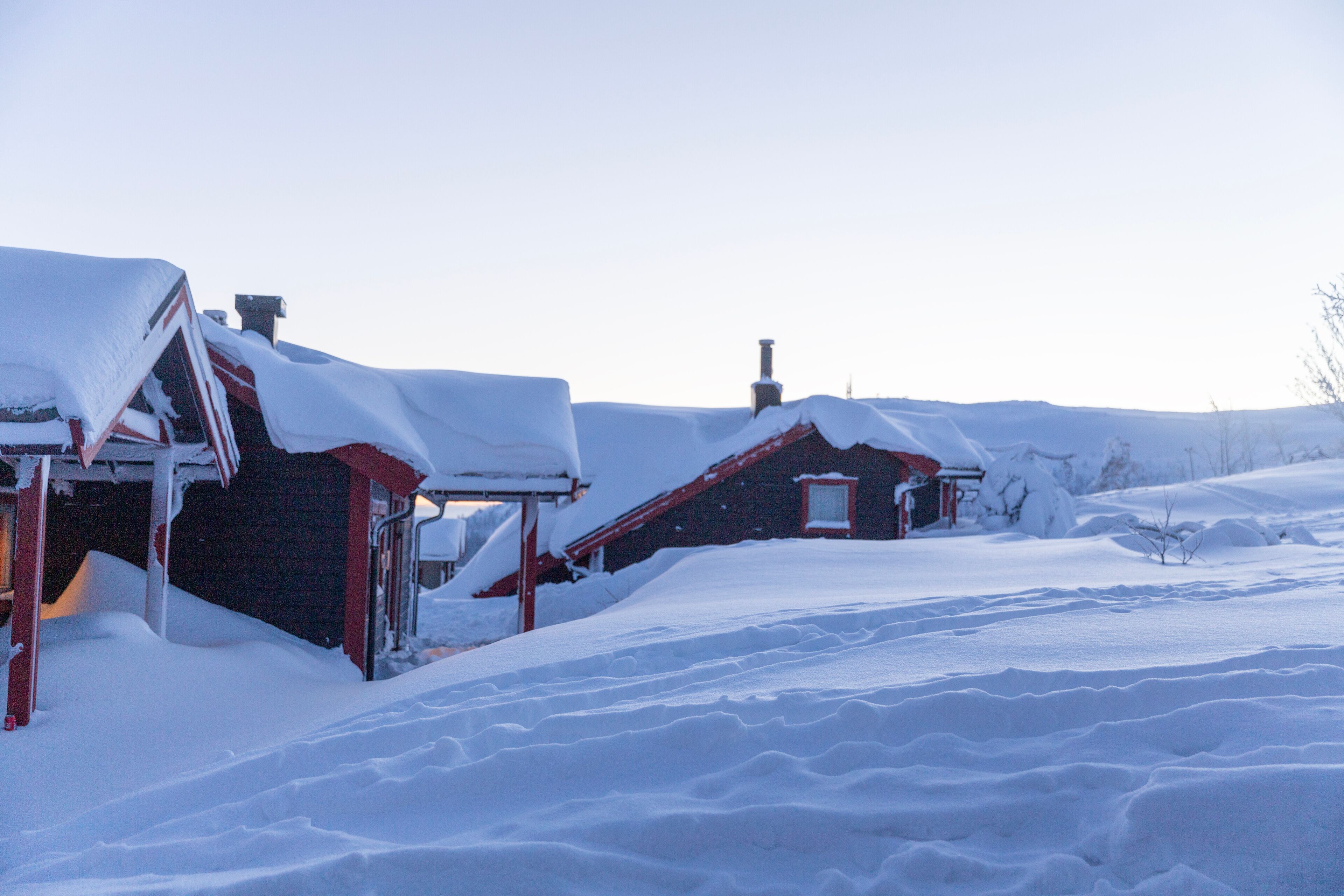 A snowy landscape with two red-roofed buildings partially covered in snow.