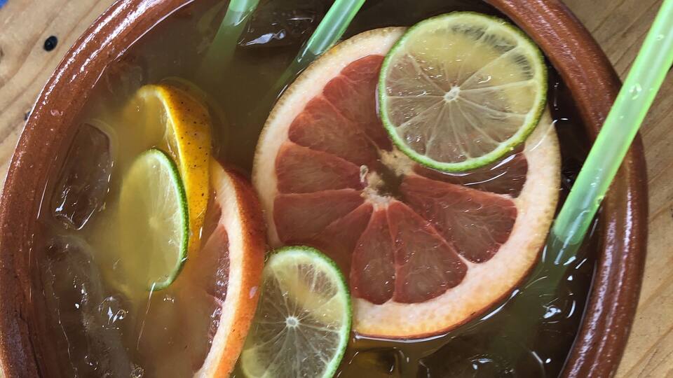 A bowl of clear liquid with slices of citrus and green stalks.