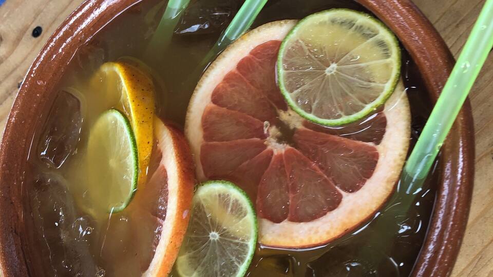 A ceramic bowl filled with a clear liquid, containing slices of citrus and green stalks.