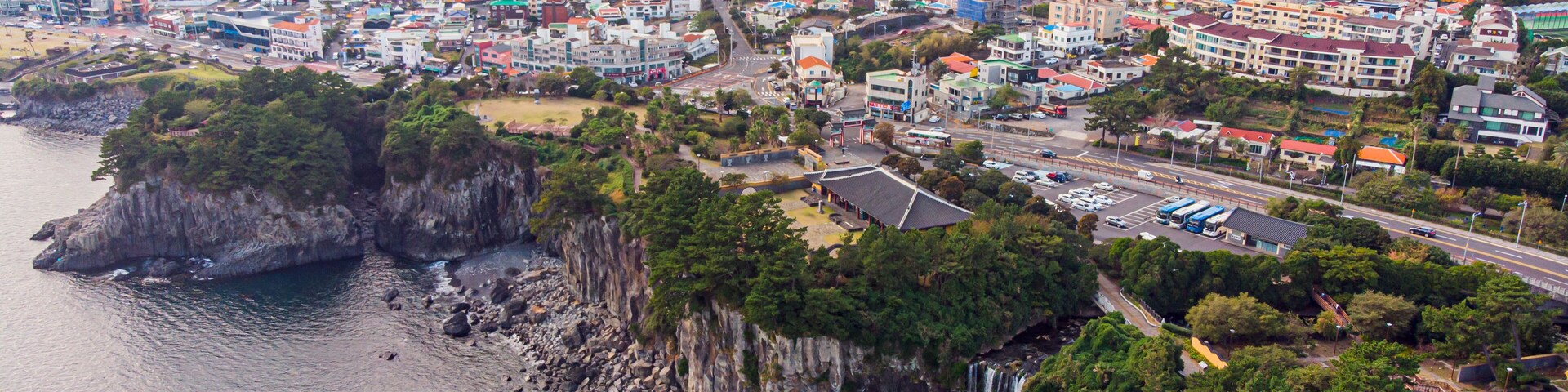 Un paisaje urbano costero con una cascada destacada, acantilados rocosos y una combinación de edificios residenciales y comerciales.