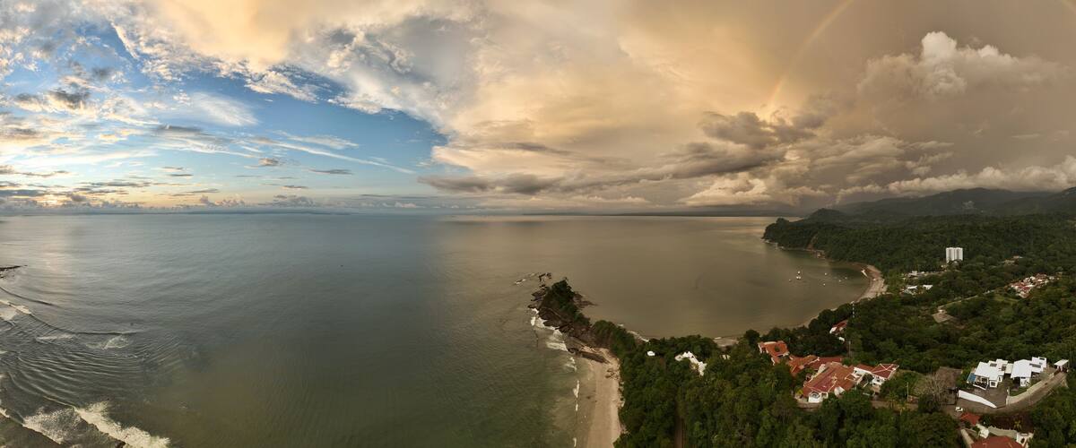A coastal landscape with a beach, a forested area, and a distant mountain range.