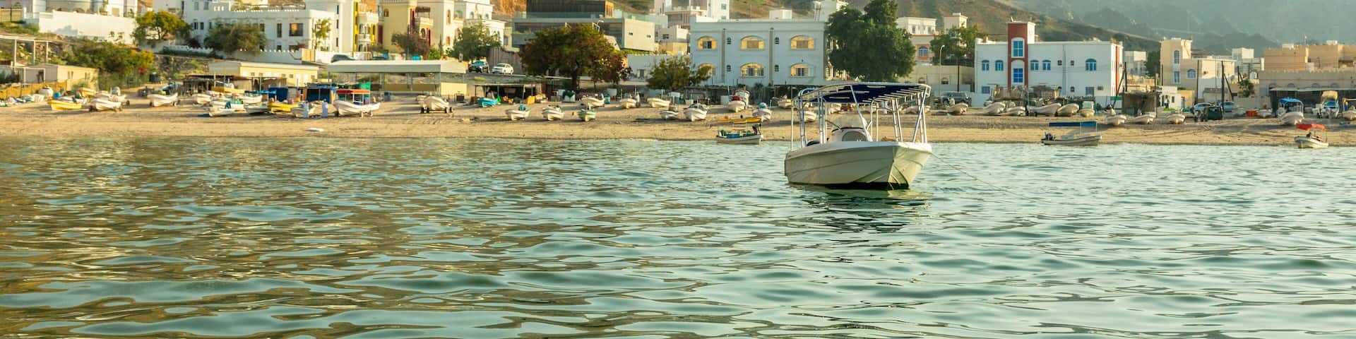 Al-Bustan village white houses on the shore view from the sea bay with mountains in the background, Muscat, sultanate Oman