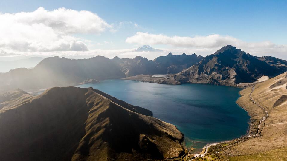 A mountainous landscape with a large lake surrounded by rugged terrain and distant snow-capped peaks.