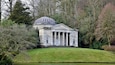 A classical building with a dome and columns, surrounded by trees and a grassy area.