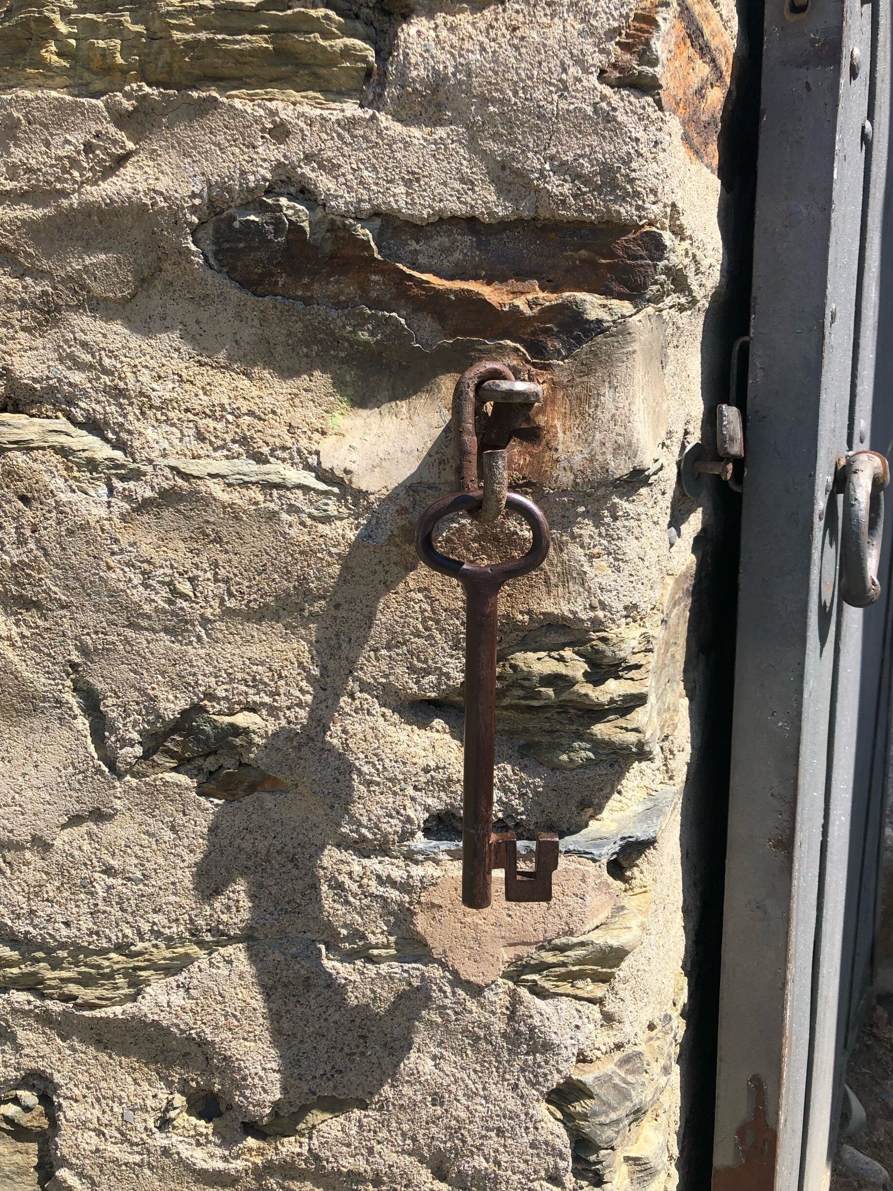 An old rusty key attached to a stone wall.