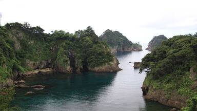 A coastal landscape with a narrow waterway flanked by lush green cliffs and a sandy beach.