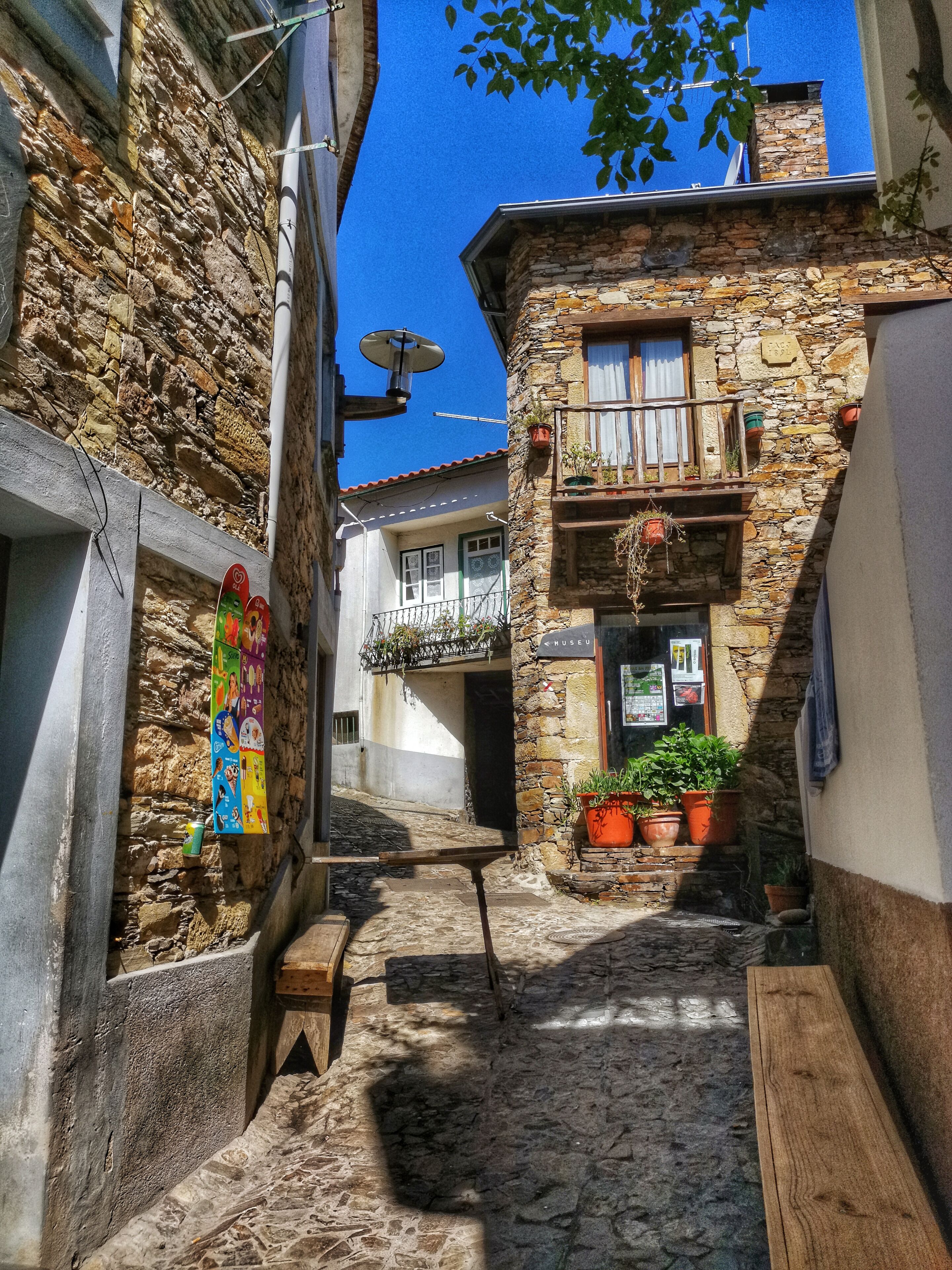 A narrow cobblestone alley with stone buildings, a wooden bench, and potted plants.