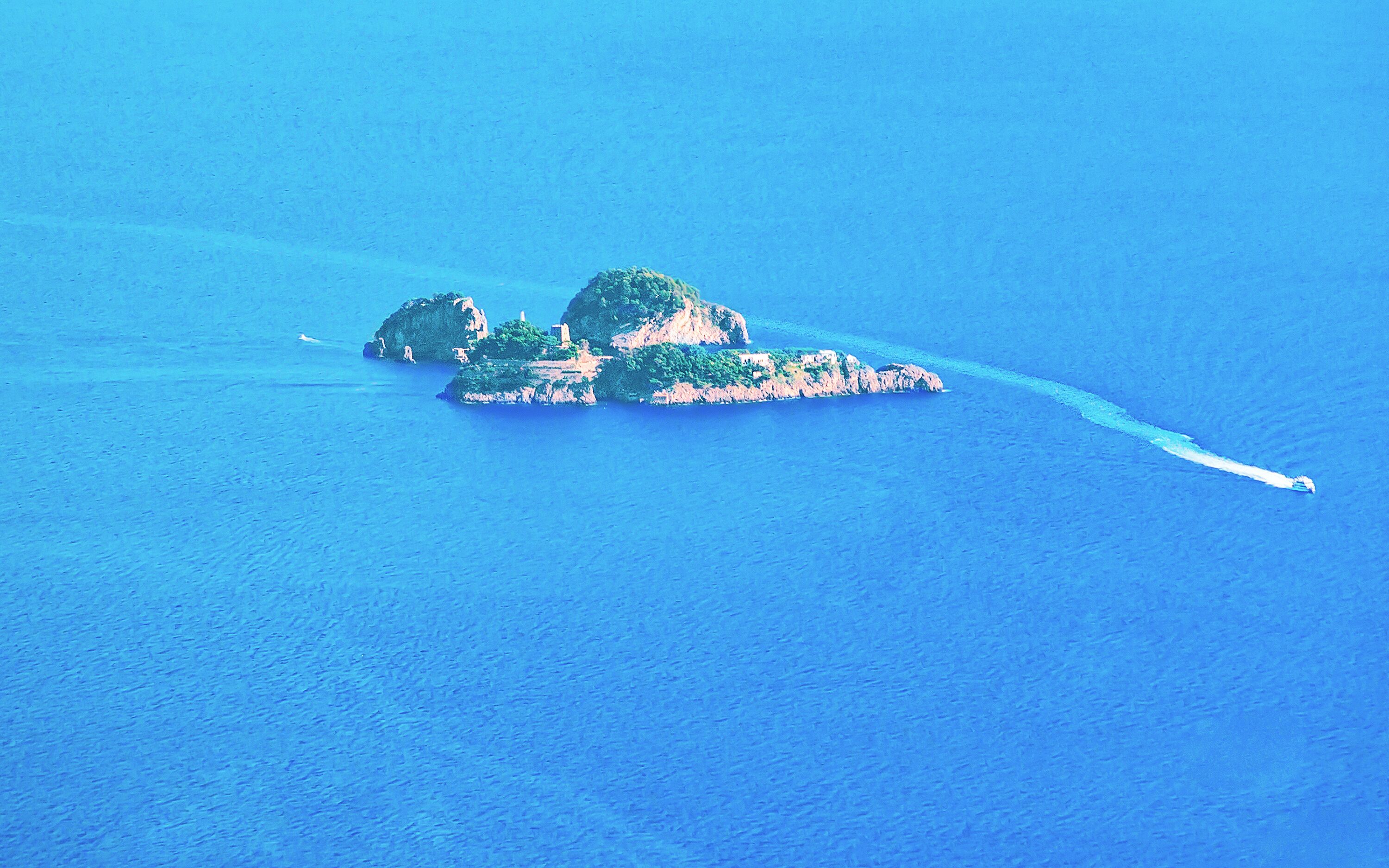 An aerial view of a small island with lush greenery and rocky outcrops surrounded by deep blue water.