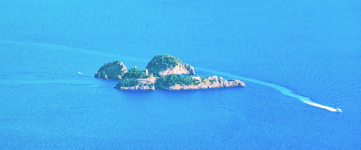 An aerial view of a small island with lush greenery and rocky outcrops surrounded by deep blue water.