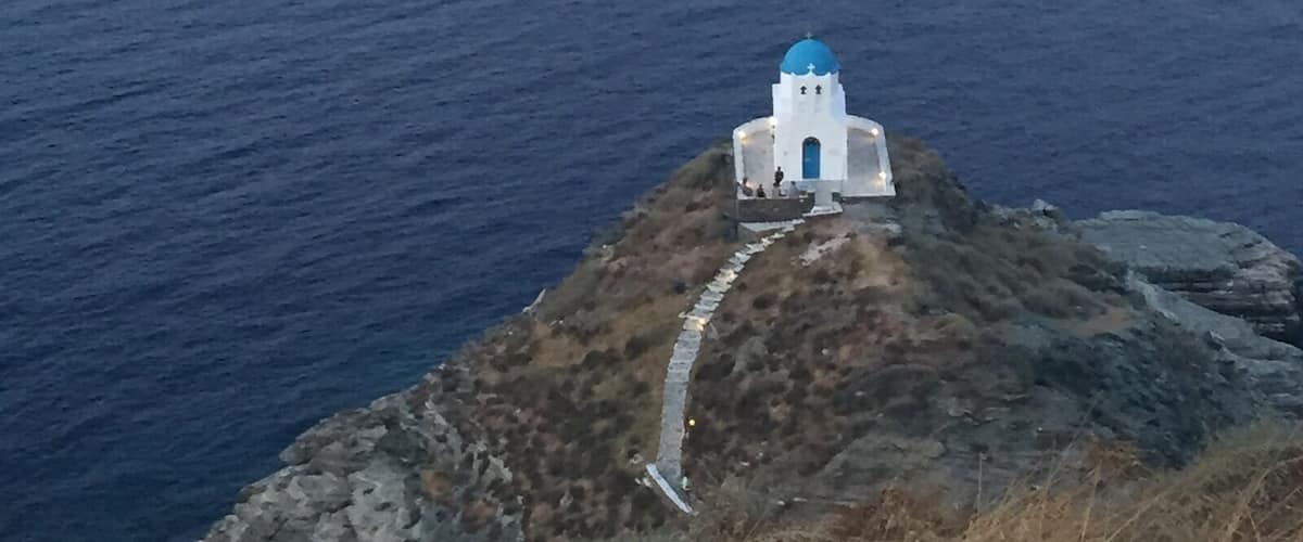 A white building with a blue dome on a rocky cliff overlooking the sea.