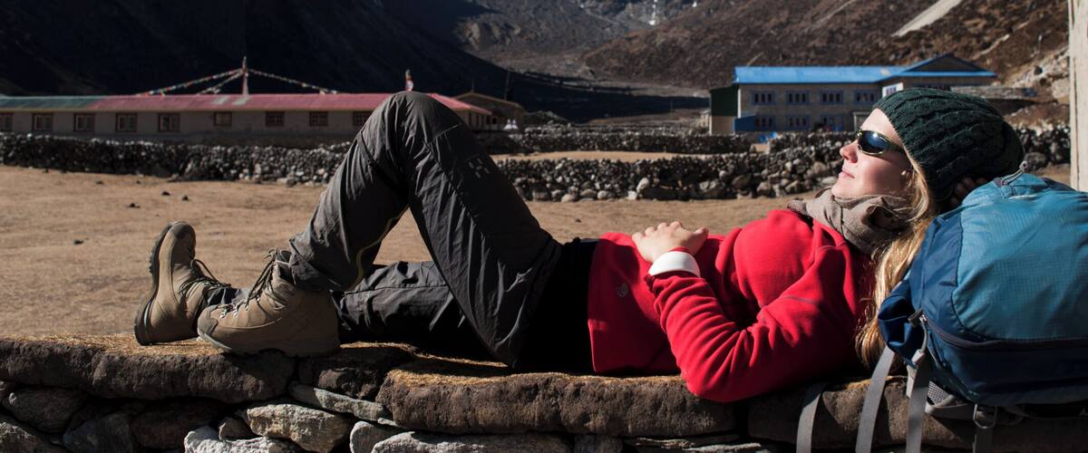 A person lying on a stone wall with a mountainous landscape in the background.