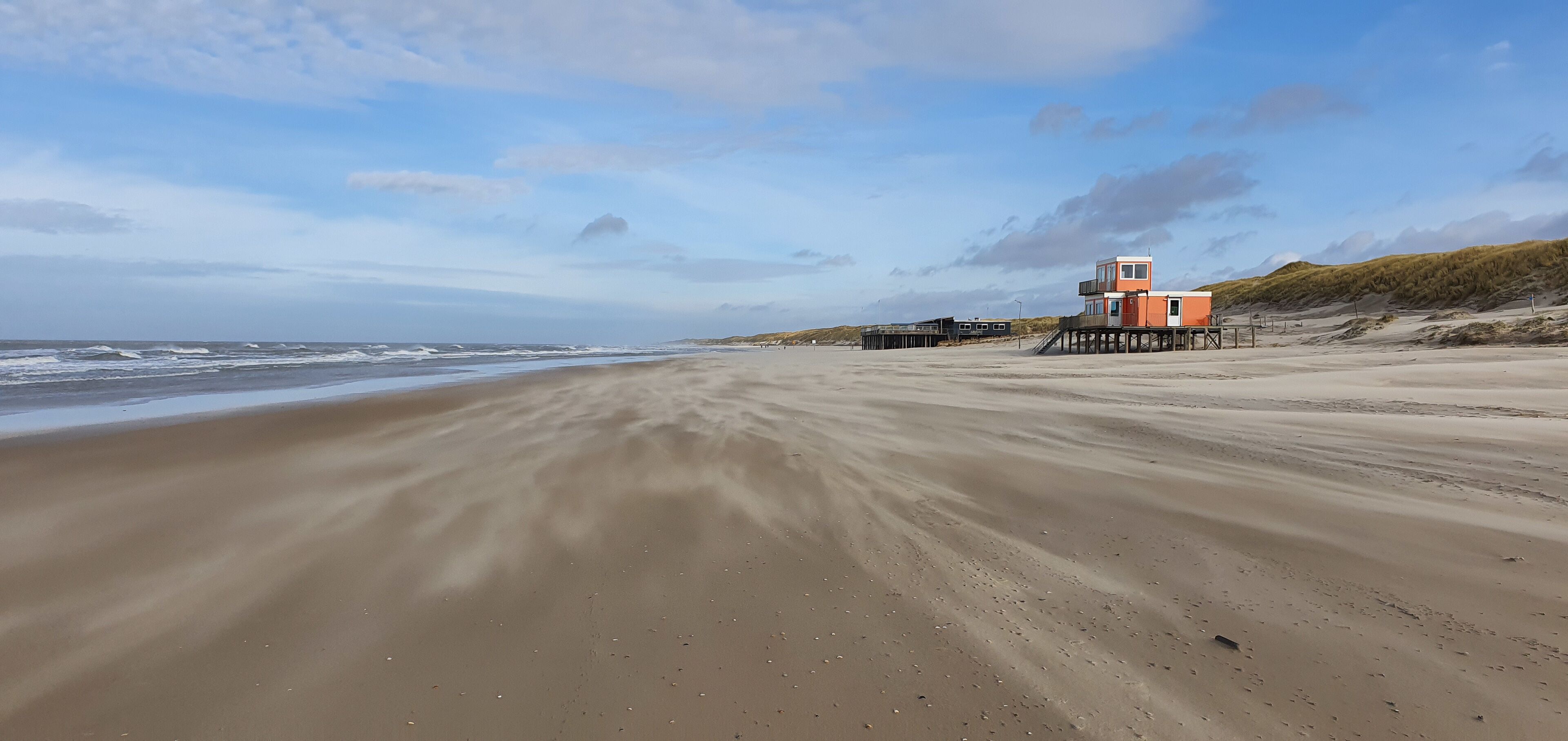 A sandy beach with a lifeguard tower and a pier extending into the water.