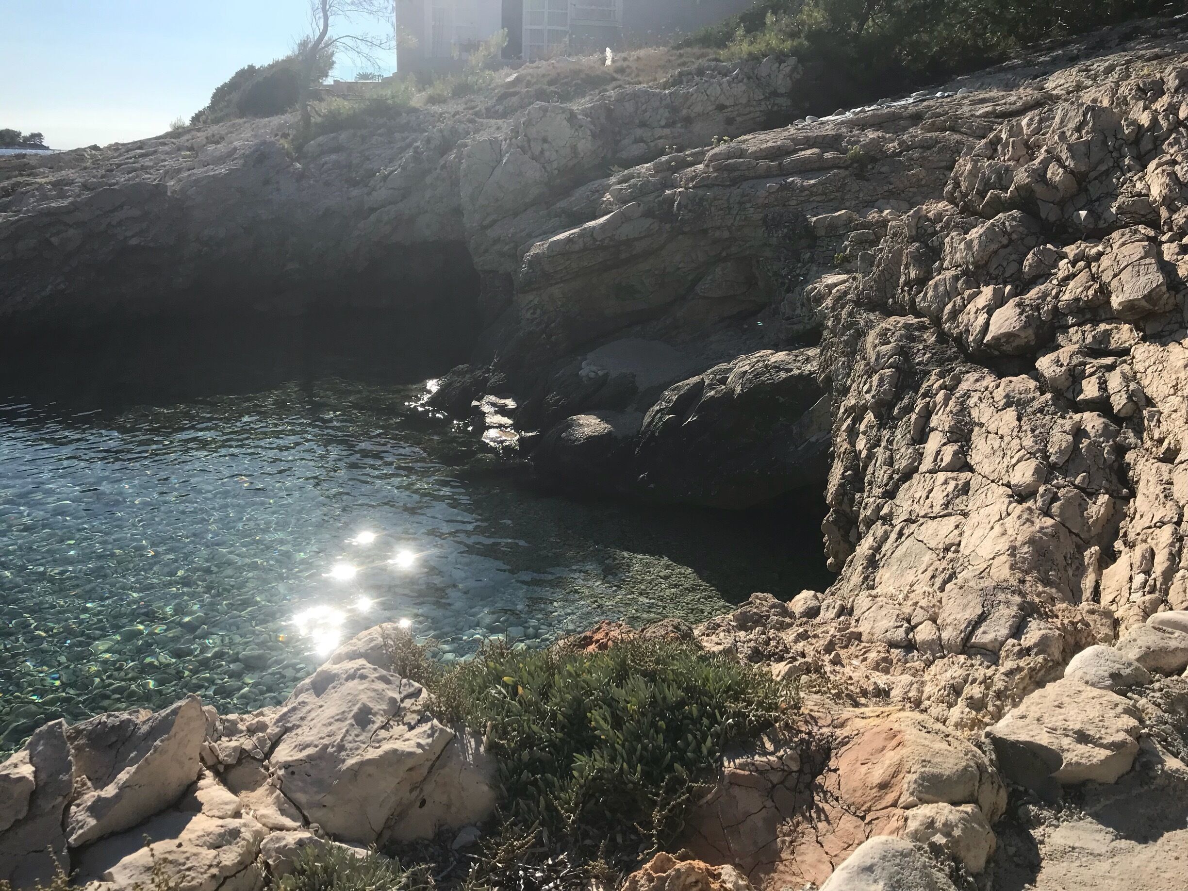 A rocky coastline with clear water and sunlight reflecting off the surface.