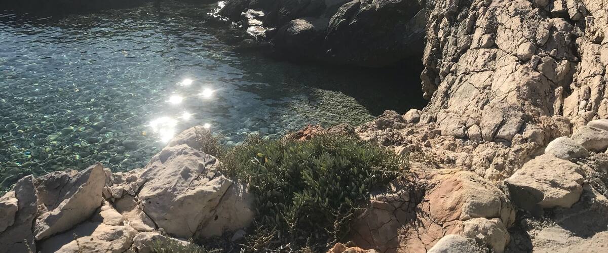 A rocky coastline with clear water and sunlight reflecting off the surface.