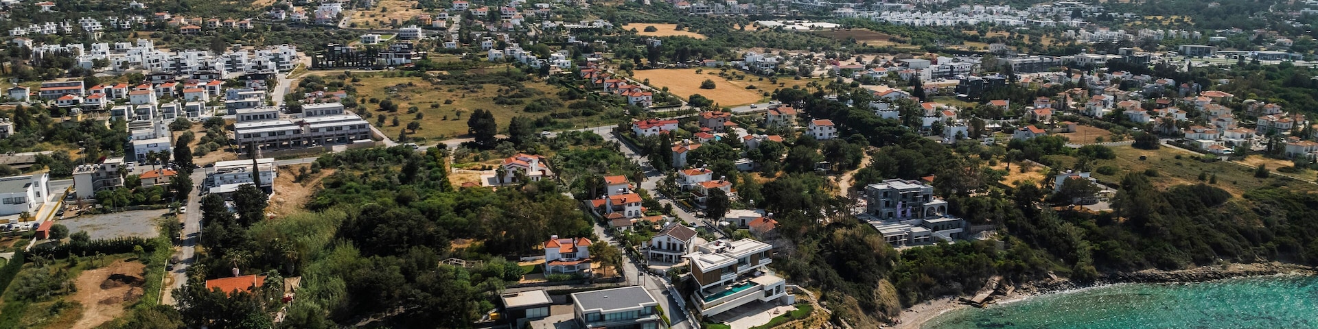 Aerial view of beautiful sandy beach and coastal village with homes and mountains, Agios Georgios Keryneias, Kyrenia, Turkish Republic of Northern Cyprus.