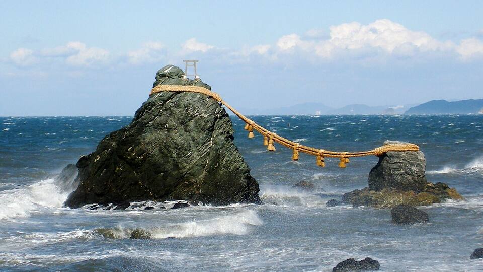A rocky coastline with a rope tied around a large rock and a smaller rock in the sea.