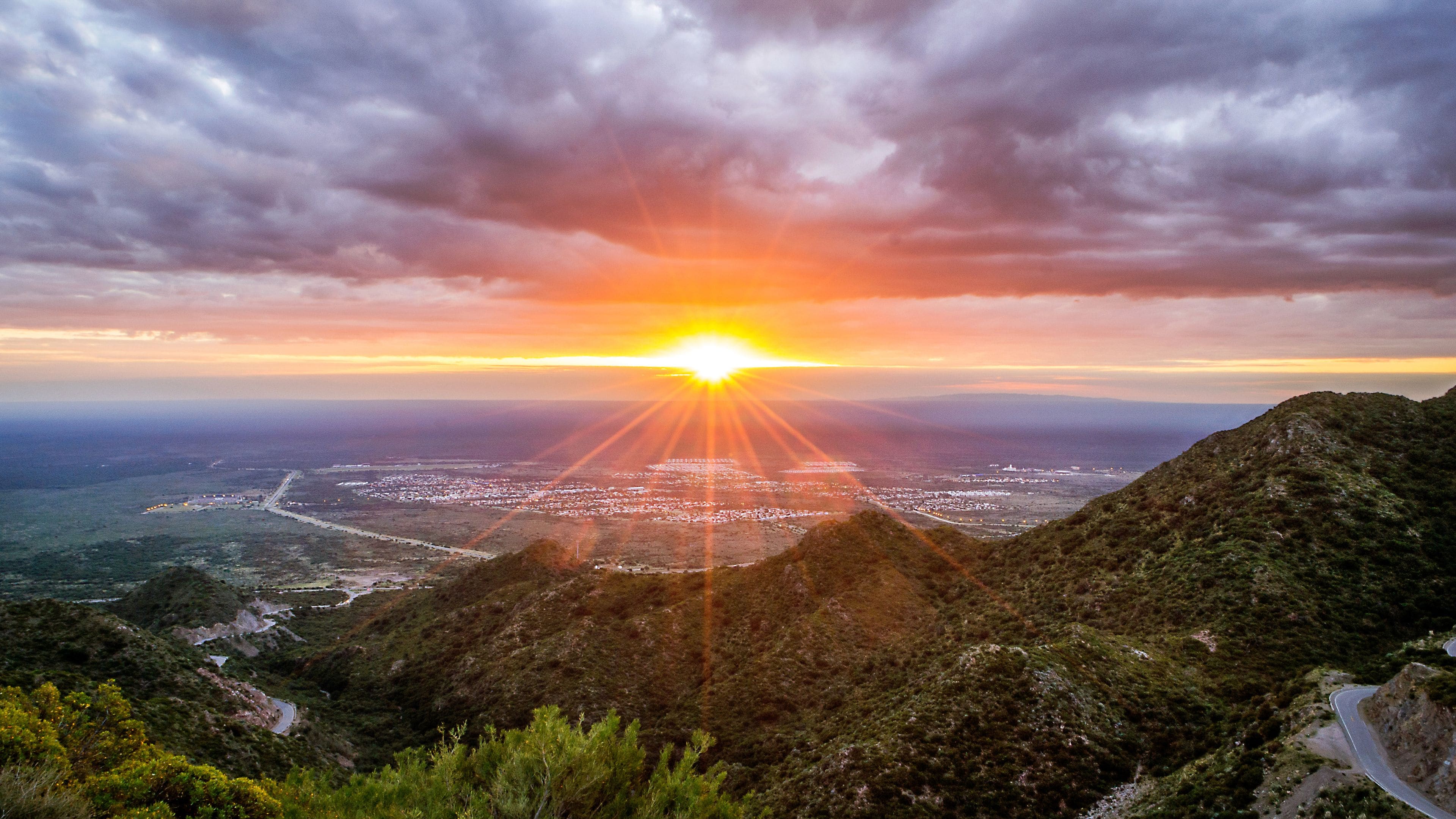 A sunset over a coastal city with a mountainous backdrop.