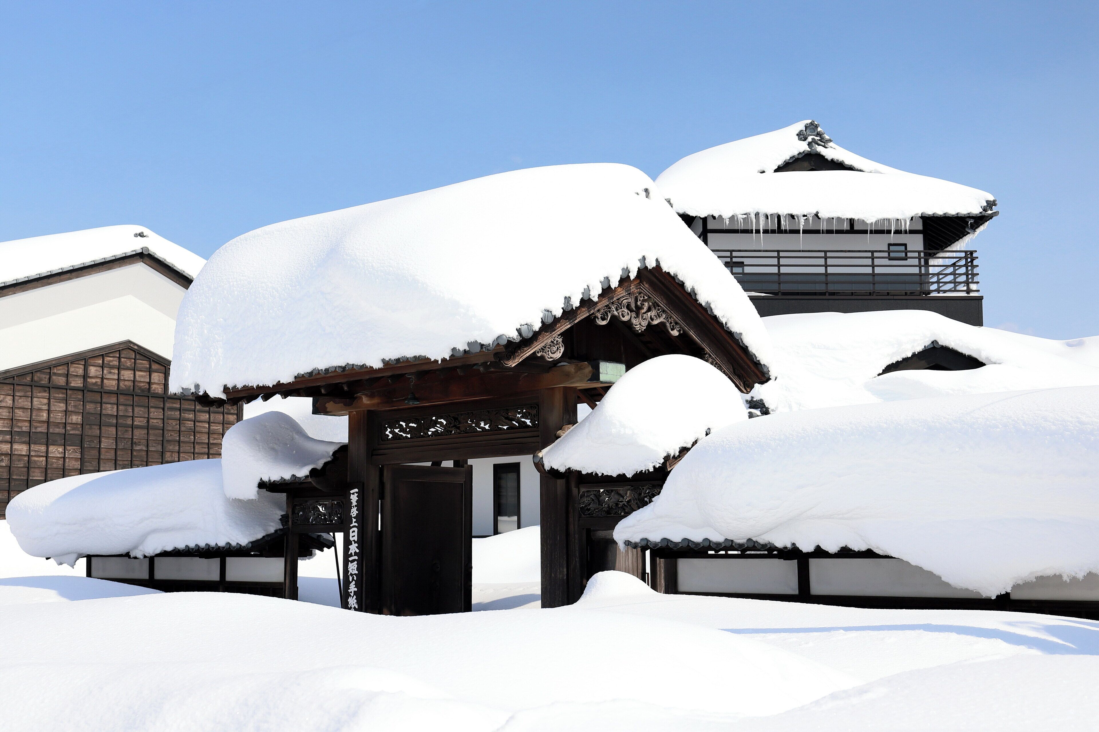 A traditional Japanese building covered in snow with a clear blue sky in the background.