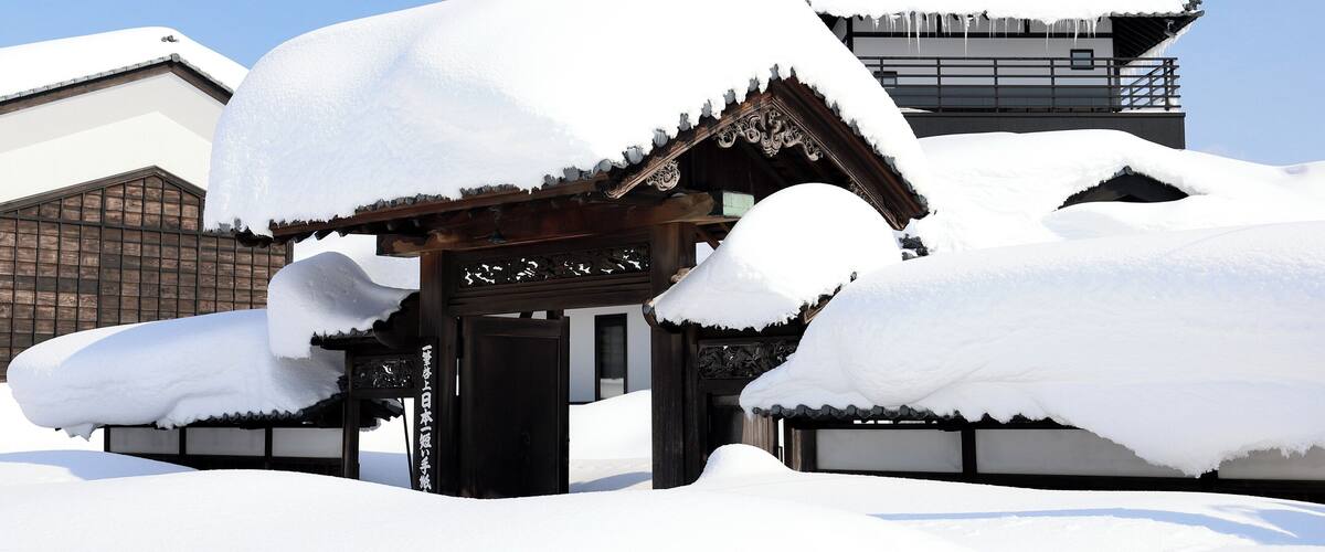 A traditional Japanese building covered in snow with a clear blue sky in the background.
