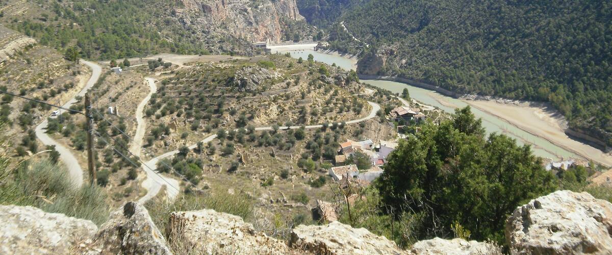 A mountainous landscape with a winding river, rocky terrain, and scattered buildings.