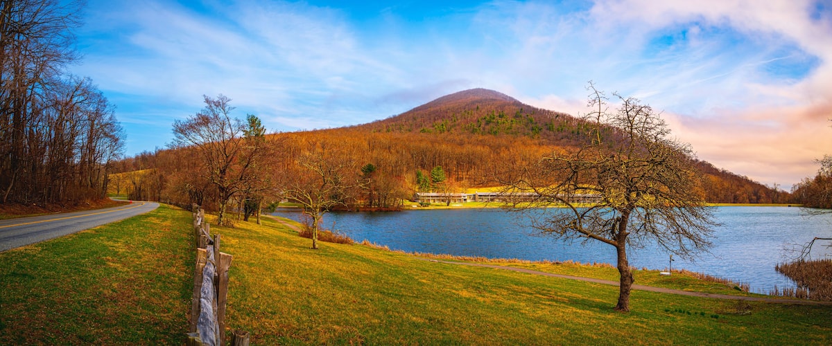 A lake with a mountain in the background, surrounded by trees and a road.