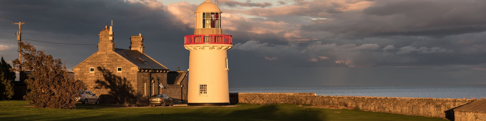 Ballinacourty lighthouse lit by the setting sun with the sea and dark clouds in the background. Ballinacourty, County Waterford, Republic of Ireland.