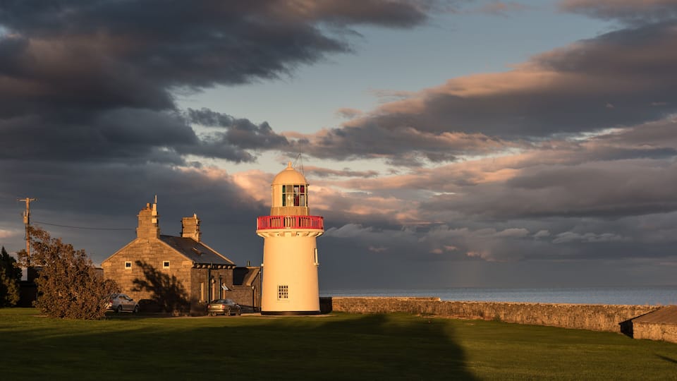 Ballinacourty lighthouse lit by the setting sun with the sea and dark clouds in the background. Ballinacourty, County Waterford, Republic of Ireland.