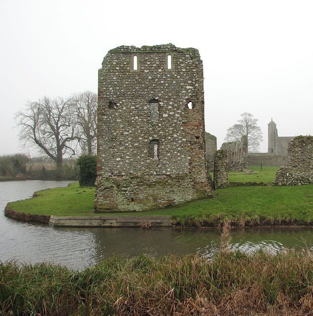 Una torre de piedra medieval junto a un río, rodeada de campos verdes y una iglesia distante.