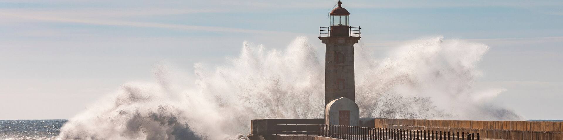A lighthouse by a turbulent sea with waves crashing against the pier.