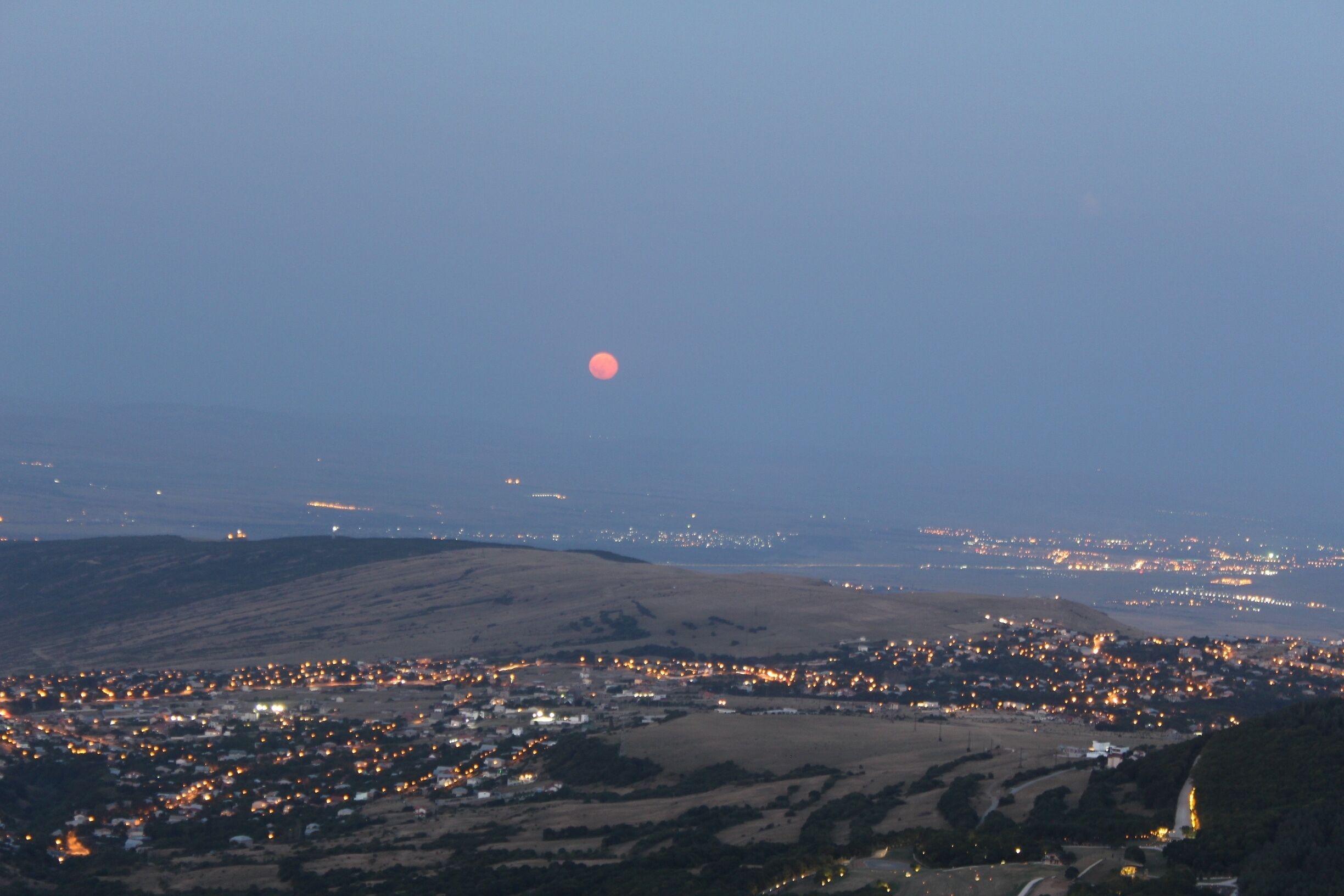 A city at dusk with a visible moon in the sky and distant lights.