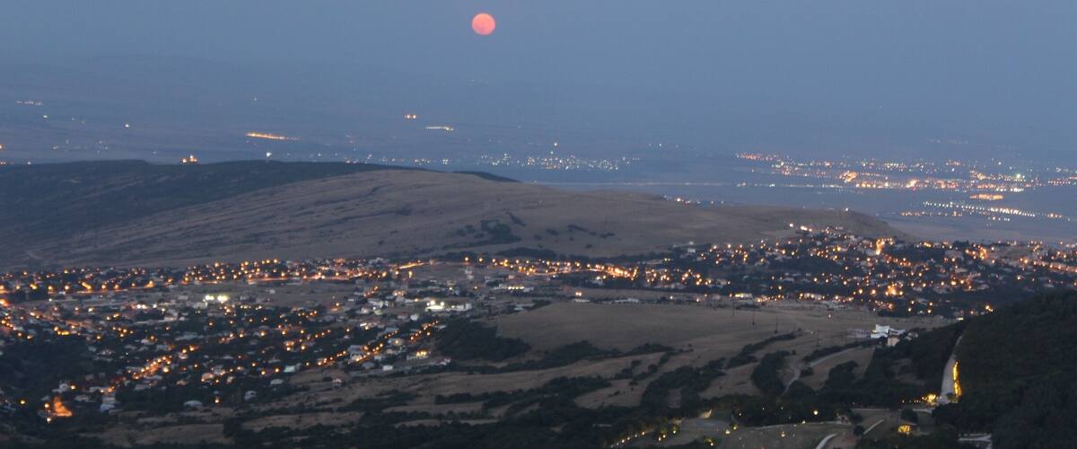 A city at dusk with a visible moon in the sky and distant lights.