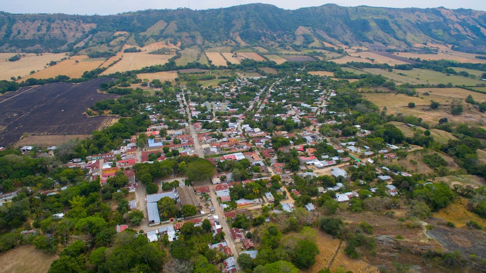 An aerial view of a town with a central road, surrounded by fields and hills.