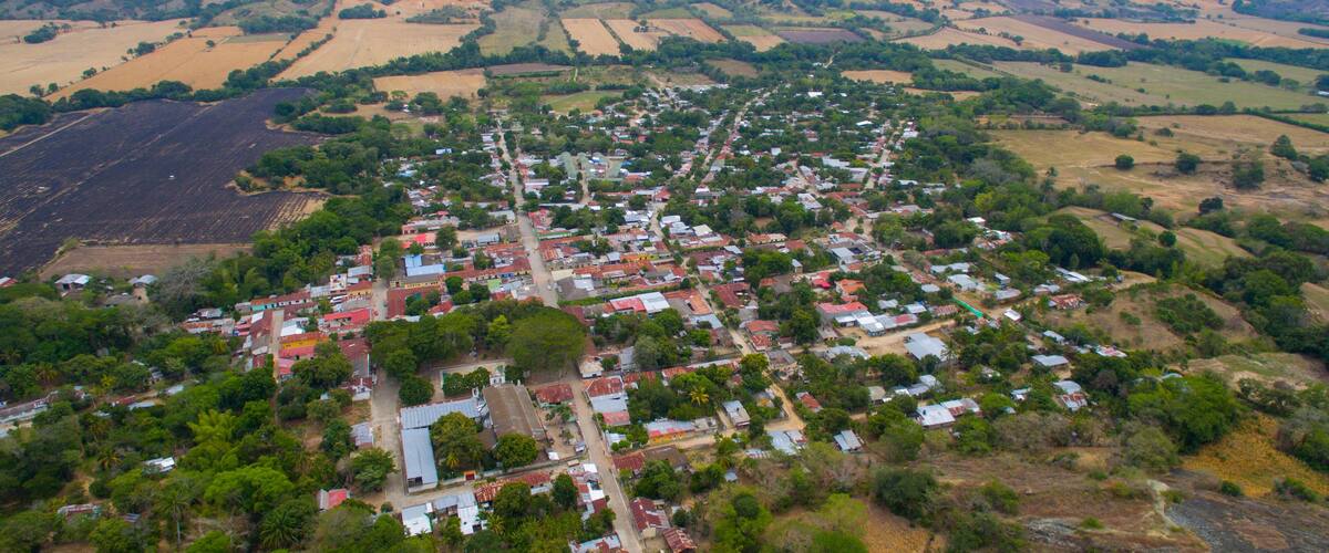 An aerial view of a town with a central road, surrounded by fields and hills.