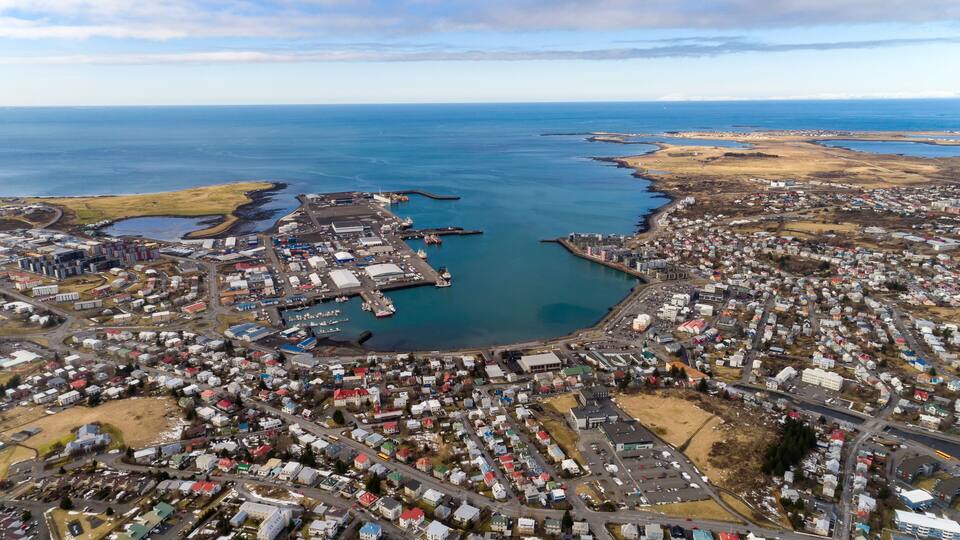 An aerial view of a coastal town with a harbor, residential areas, and a large body of water.