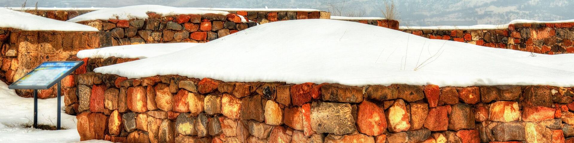 A stone wall with a snow-covered roof and a sign in a snowy landscape.