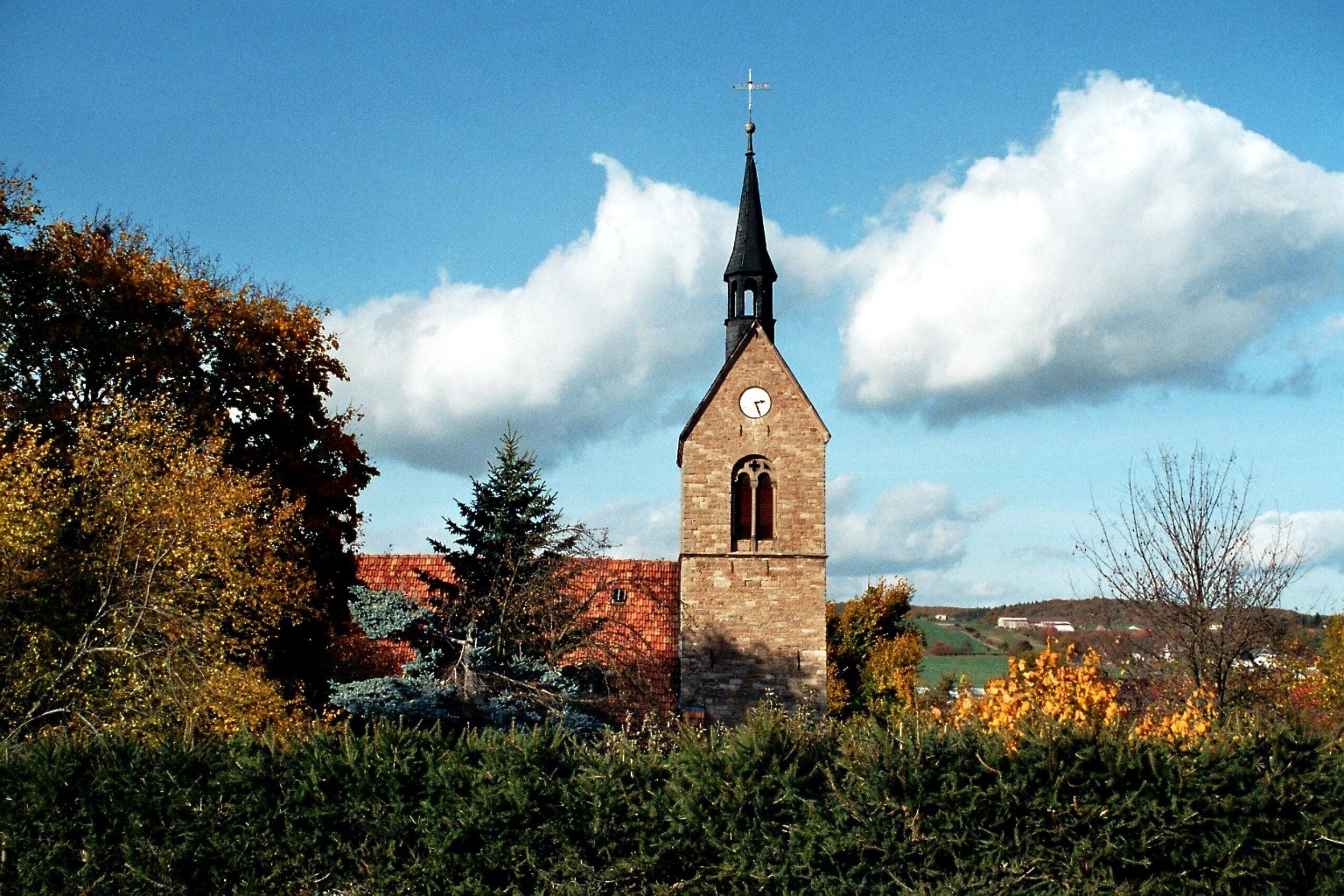 A church with a clock tower, surrounded by autumn foliage and a clear sky.