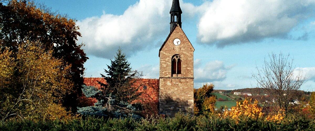 A church with a clock tower, surrounded by autumn foliage and a clear sky.