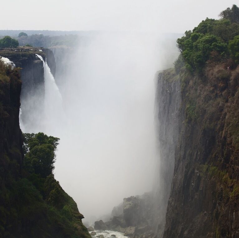 A large waterfall cascading down a steep cliff surrounded by dense vegetation.